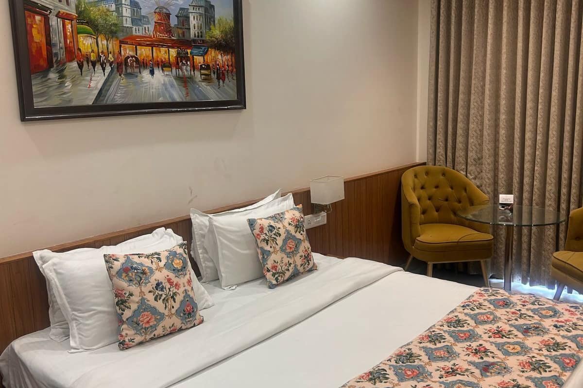 A hotel room with a bed, a painting, a chair, and a window with curtains.