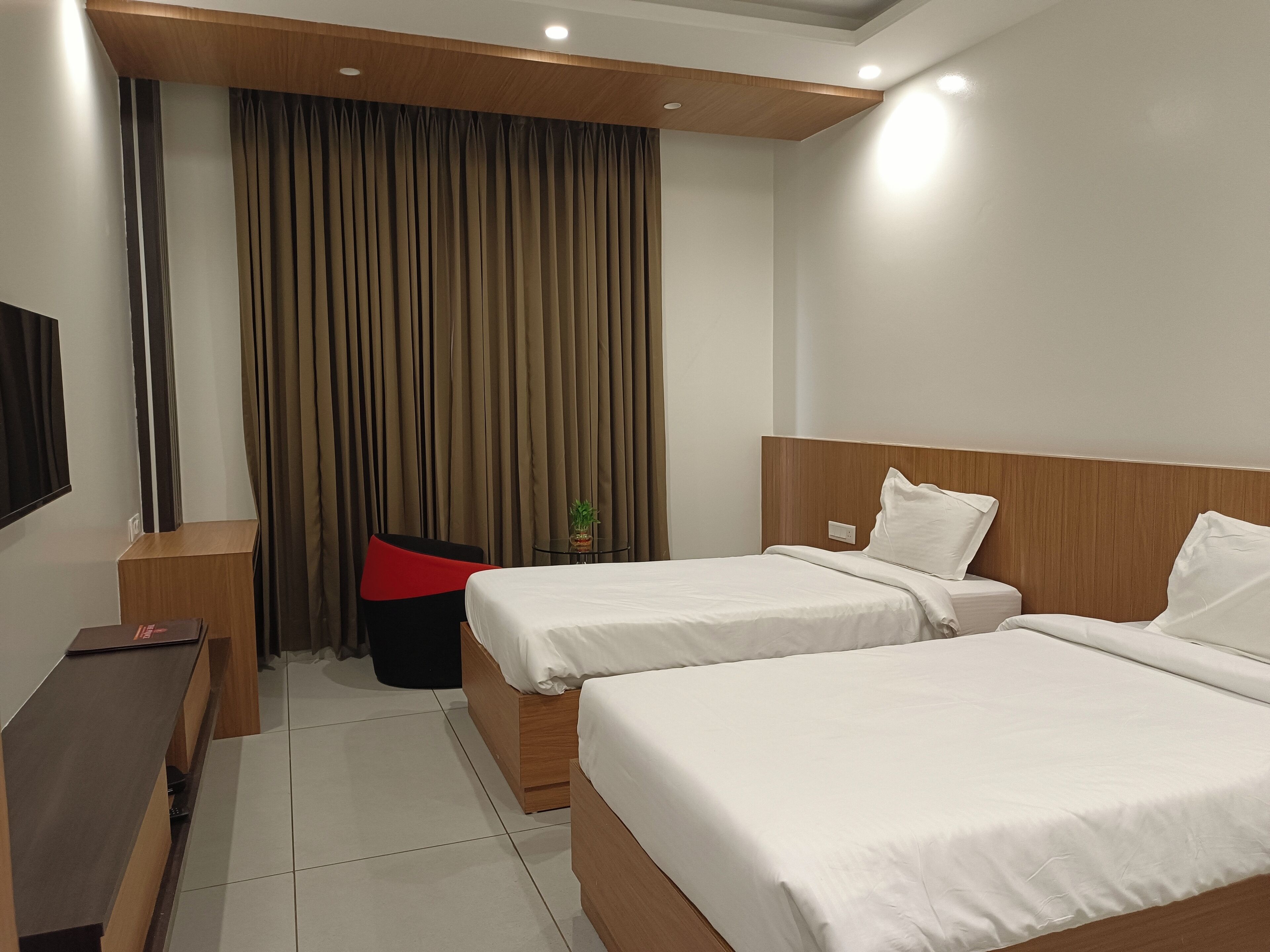A hotel room with two beds, a desk, a chair, and a TV.