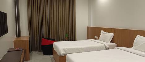 A hotel room with two beds, a desk, a chair, and a TV.