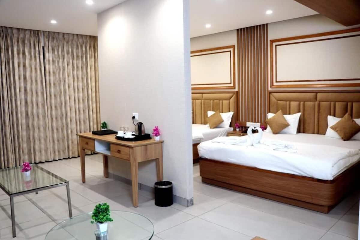 A hotel room with a wooden desk, a glass table, a bed with white bedding, and a large window with curtains.