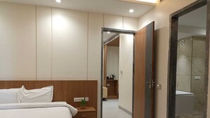 A modern hotel room with a large bed, a wooden nightstand, a small plant, and a bathroom visible through an open door. - THE PRINCE ZENQ XPRESS RESORTT ROHTAK (Sampla)