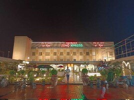 Un hotel con fachada moderna, señalización de 'The Prince' y 'Zeno Xpress', y un área de entrada bien iluminada con plantas en macetas.