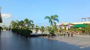 An outdoor plaza with tiled flooring, palm trees, and outdoor seating areas with umbrellas. - THE PRINCE ZENQ XPRESS RESORTT ROHTAK (Sampla)