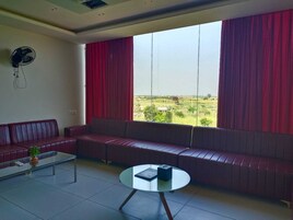 Un salón moderno con un sofá rojo, una mesa de centro de cristal y vistas a un paisaje verde a través de amplias ventanas con cortinas rojas.