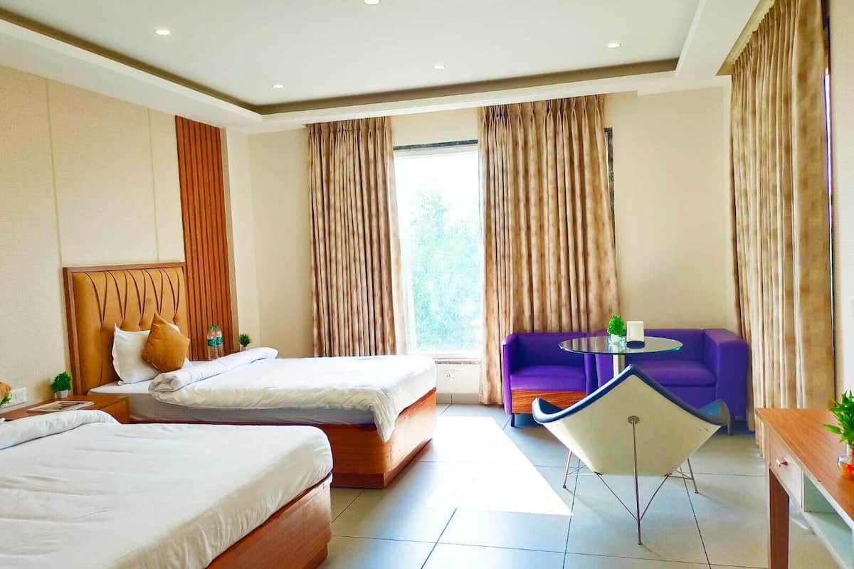 A hotel room with two beds, a purple sofa, a small table, and a chair.