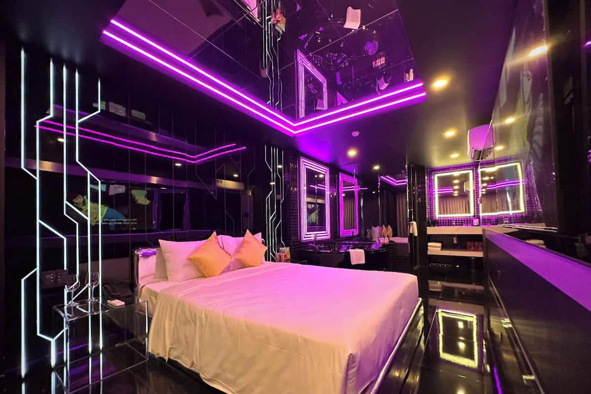 Een moderne hotelkamer met een groot bed, een kaptafel met spiegels en neonverlichting.