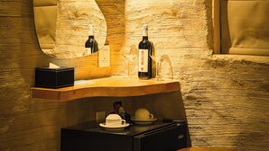 A bathroom with a wooden vanity, a mirror, a bottle of wine, a cup, and a small refrigerator.