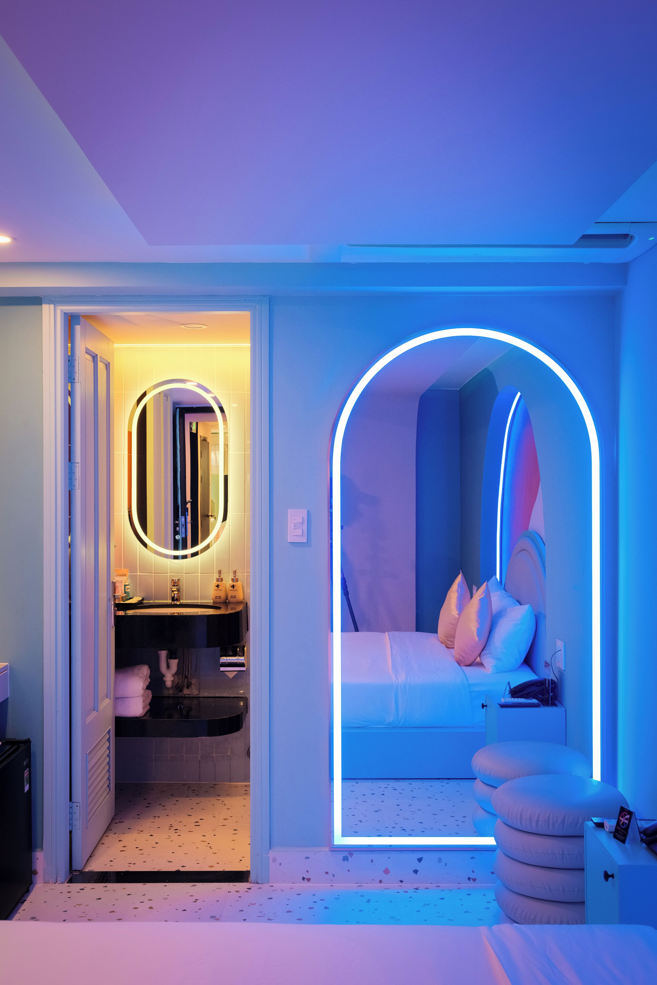 Un dormitorio moderno con cama, mesita de noche y espejo con marco iluminado.