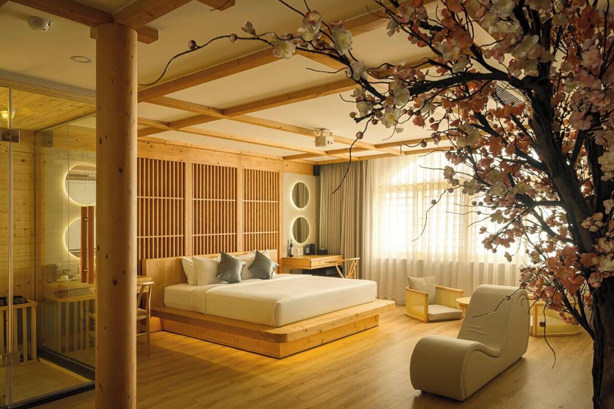Een moderne slaapkamer met een groot bed, een zithoek en een decoratieve boom.
