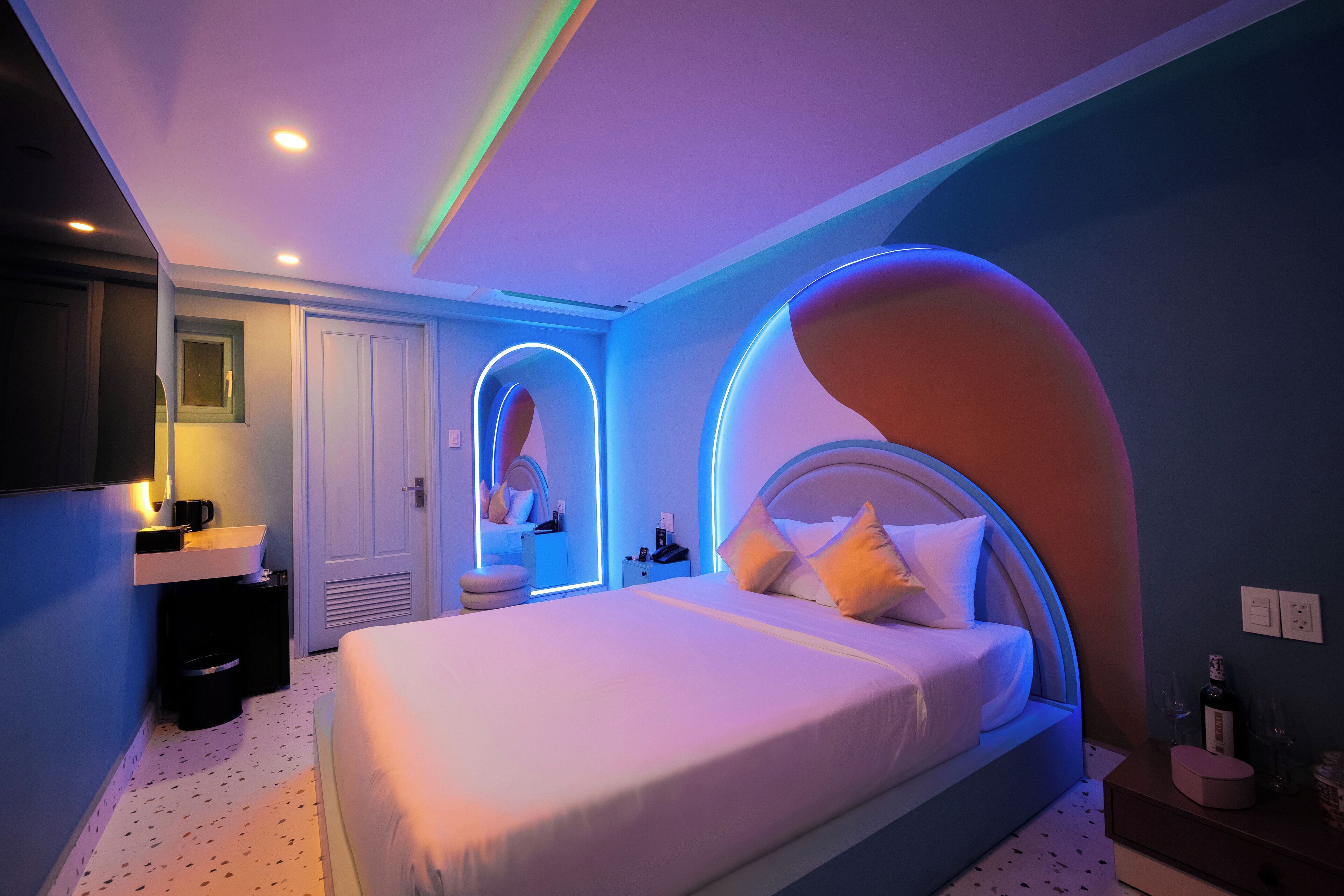 A modern bedroom with a large bed, a bedside table, a nightstand, and a mirror.