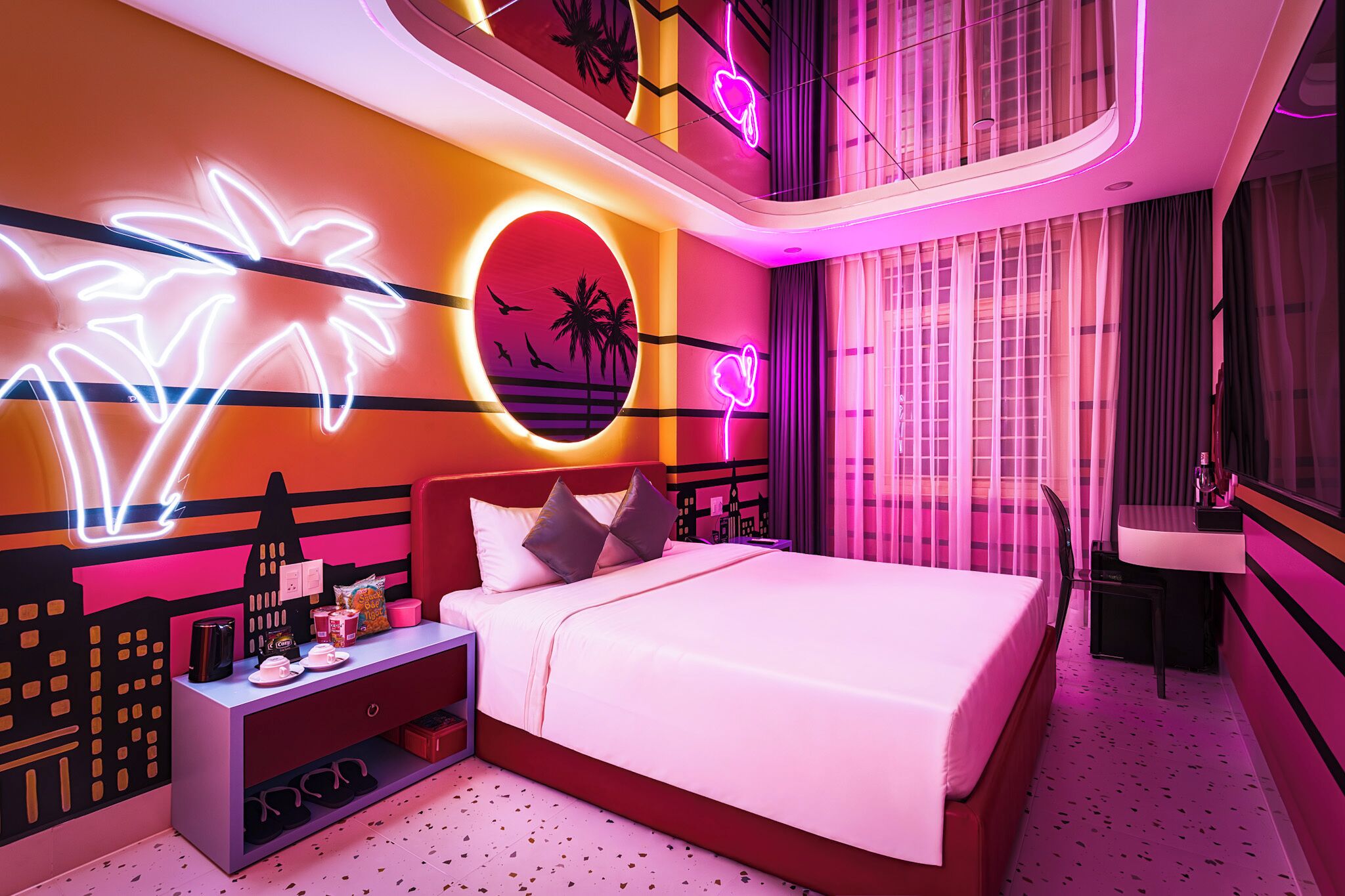 A modern hotel room with a bed, nightstand, and neon wall art.