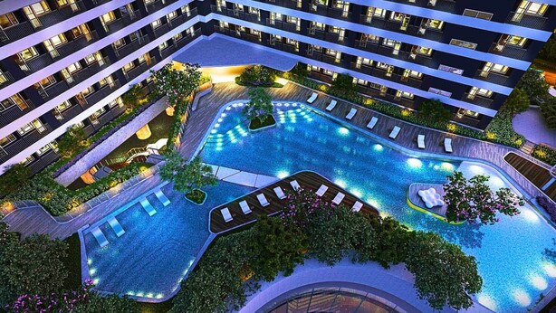 A multi-story hotel with a large, illuminated swimming pool surrounded by lush greenery and outdoor seating areas. - Rent Xpress Online Heart of Makati (Makati)