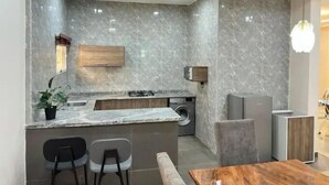 A modern kitchen with a marble backsplash, a built-in washing machine, and a wooden dining table. - Aarab Homes  (Abuja)