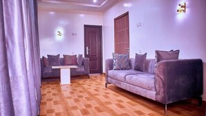A living room with a checkered wooden floor, two sofas with cushions, a coffee table, and a door. - Aarab Homes  (Abuja)