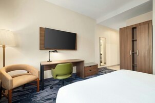 Una habitación de hotel con cama, escritorio, silla, televisor y armario.