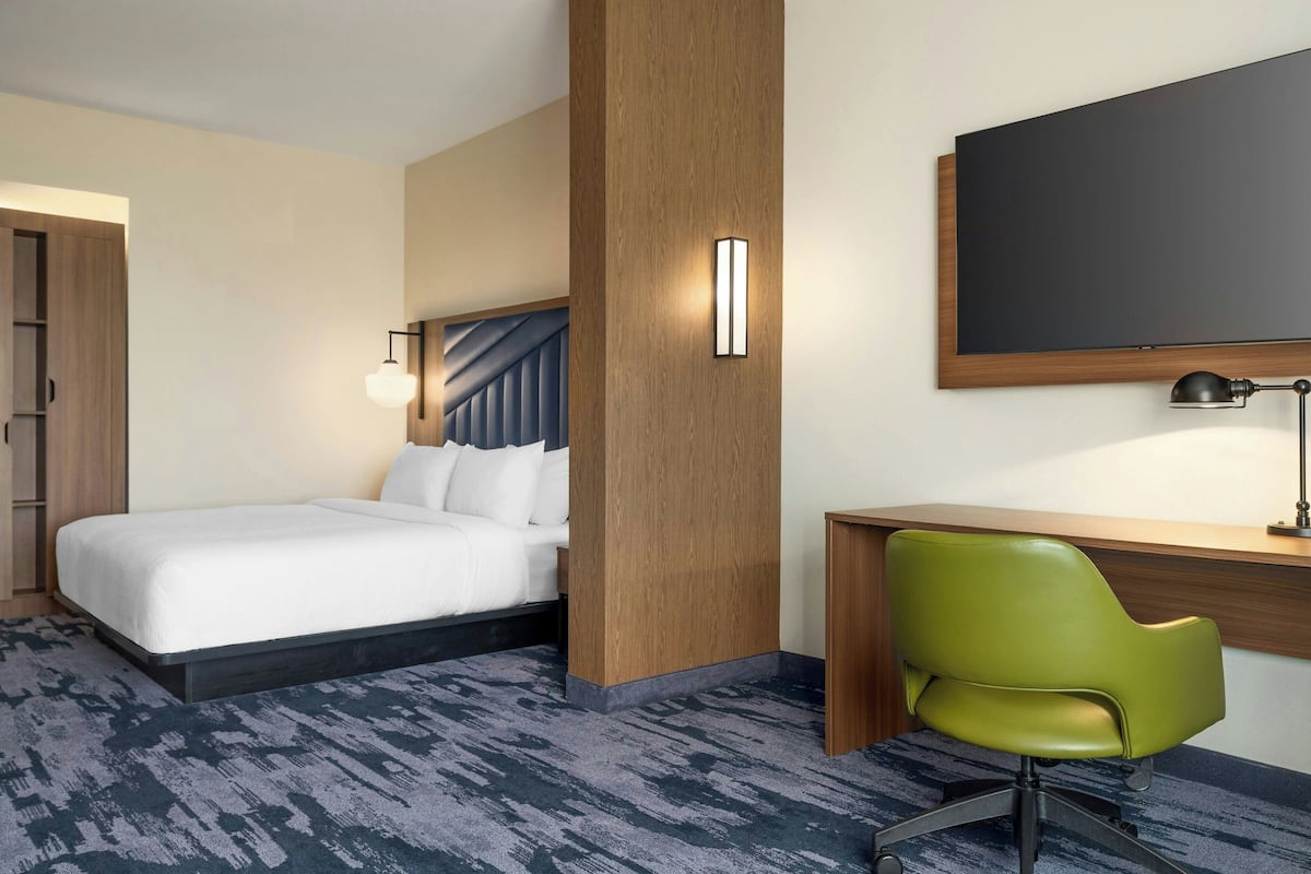 Ein Hotelzimmer mit einem Bett, einem Schreibtisch, einem Sessel, einem großen Spiegel und einem Flachbildfernseher.