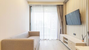 A modern living room with a sofa, a TV mounted on the wall, and a wooden console table. - Top Location Near Beach Clubs C226 (Choeng Thale)