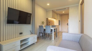 A modern living room with a flat-screen TV mounted on the wall, a dining area with a table and chairs, and a sofa. - Top Location Near Beach Clubs C226 (Choeng Thale)