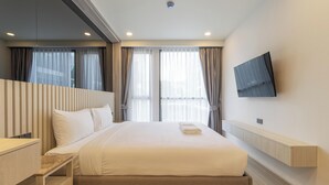 A hotel room with a large bed, a TV mounted on the wall, and a window with curtains. - Top Location Near Beach Clubs C226 (Choeng Thale)