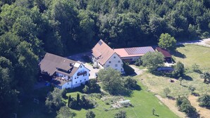 A large house with multiple sections, surrounded by a forested area. - Apartment '1' with Mountain View, Shared Garden and Wi-Fi (Owingen)