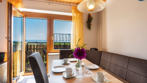 A dining area with a table set for two, a bench, and a view of the outdoors. - Apartment '1' with Mountain View, Shared Garden and Wi-Fi (Owingen)