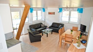A living room with a sofa, coffee table, dining table, chairs, and a TV. - Holiday Apartment '3' with Mountain View, Shared Garden and Wi-Fi (Owingen)