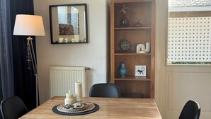 A dining area with a wooden table, black chairs, a floor lamp, a radiator, a bookshelf, and a window with blinds. - Cozy vacation home in North Holland in a very quiet park, pure relaxation! (Dirkshorn)
