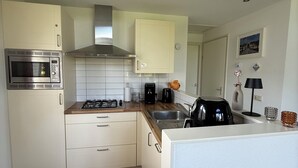 A compact kitchen with white cabinets, a microwave, a stove, and a sink. - Cozy vacation home in North Holland in a very quiet park, pure relaxation! (Dirkshorn)