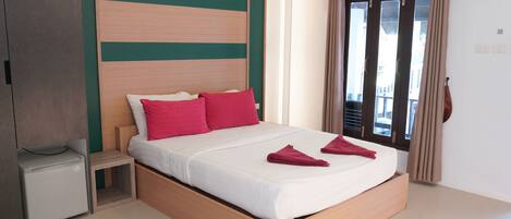 Un dormitorio moderno con estructura de cama de madera, ropa de cama blanca y almohadas rojas.