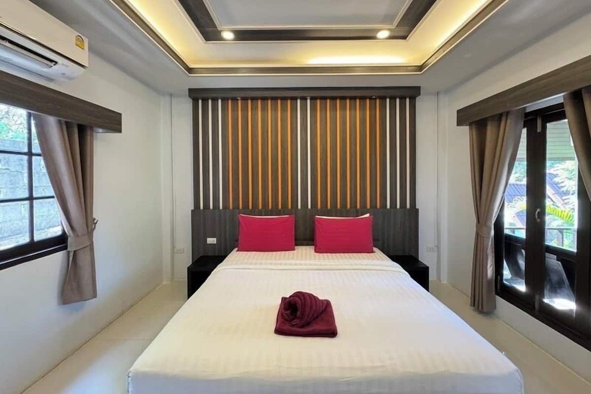 A hotel room with a large bed, two pillows, a neatly folded towel, and a striped headboard.