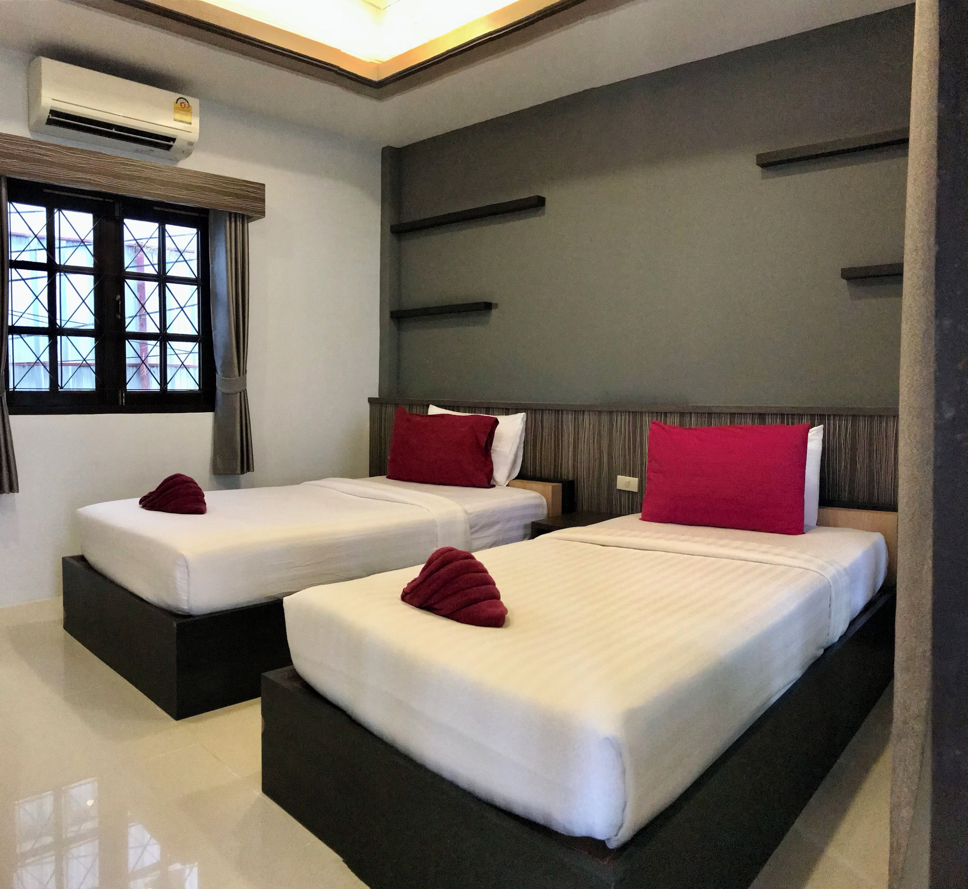 Habitación de hotel con dos camas, cada una con almohada roja y ropa de cama blanca. Se ve un edificio a través de la ventana.