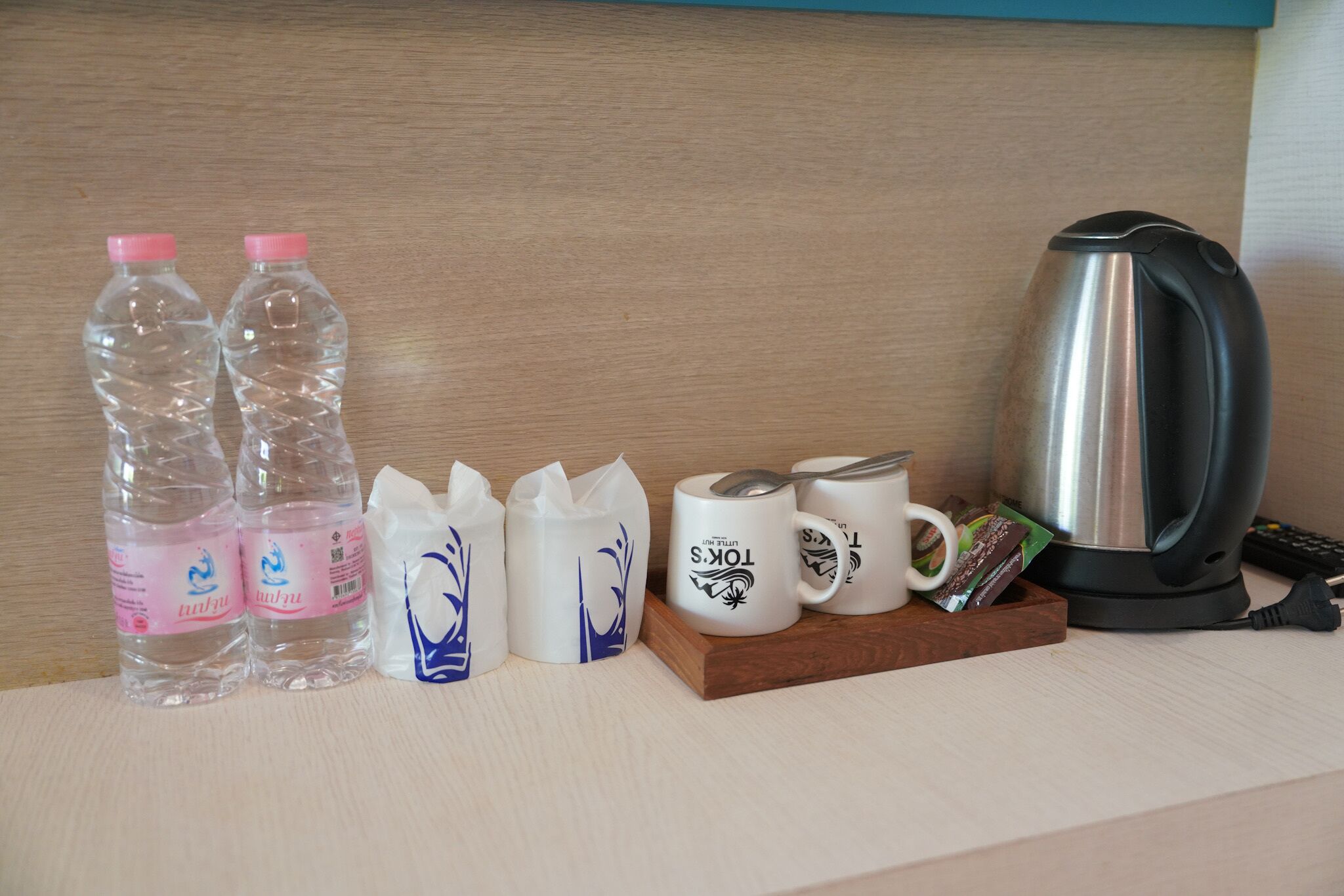 En köksbänk med vattenflaskor, en vattenkokare och kaffemuggar.