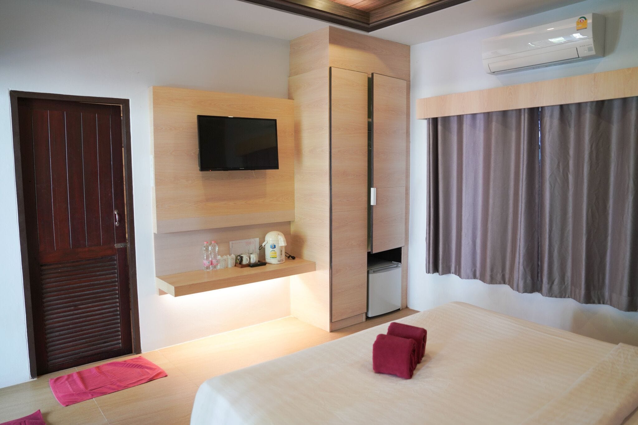 Habitación de hotel con cama, televisión montada en la pared, armario y una pequeña zona de kitchenette.