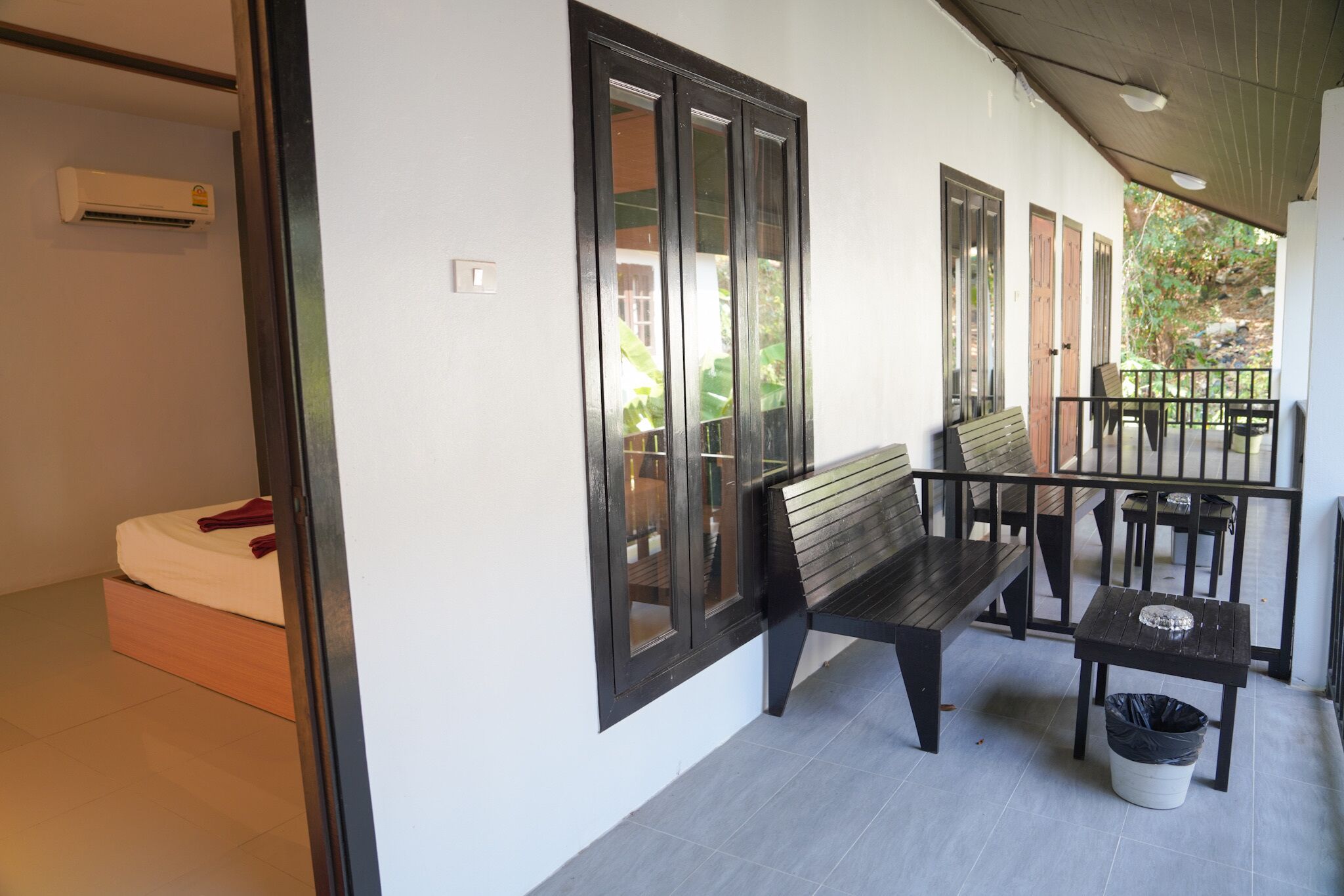 A room with a bed, a bench, a table, and a trash bin.