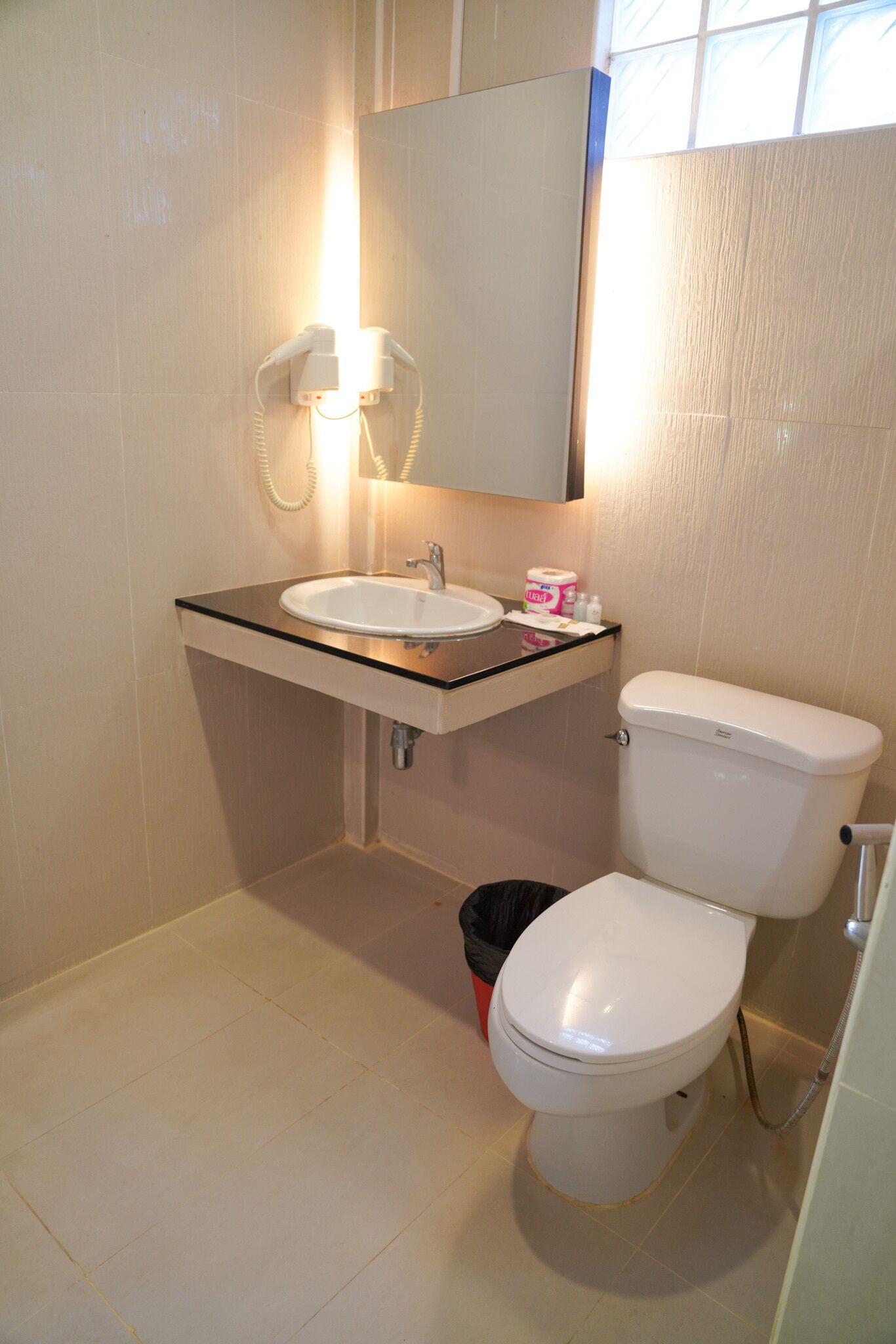 A bathroom with a white sink, mirror, and toilet. There is a trash bin and a roll of toilet paper on the counter.