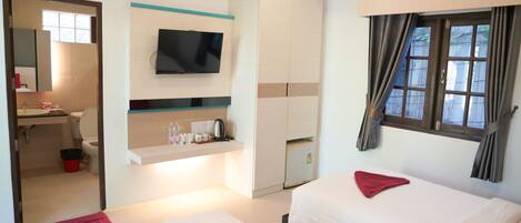 Habitación de hotel con dos camas, un televisor montado en la pared, una kitchenette pequeña y una ventana con cortinas.