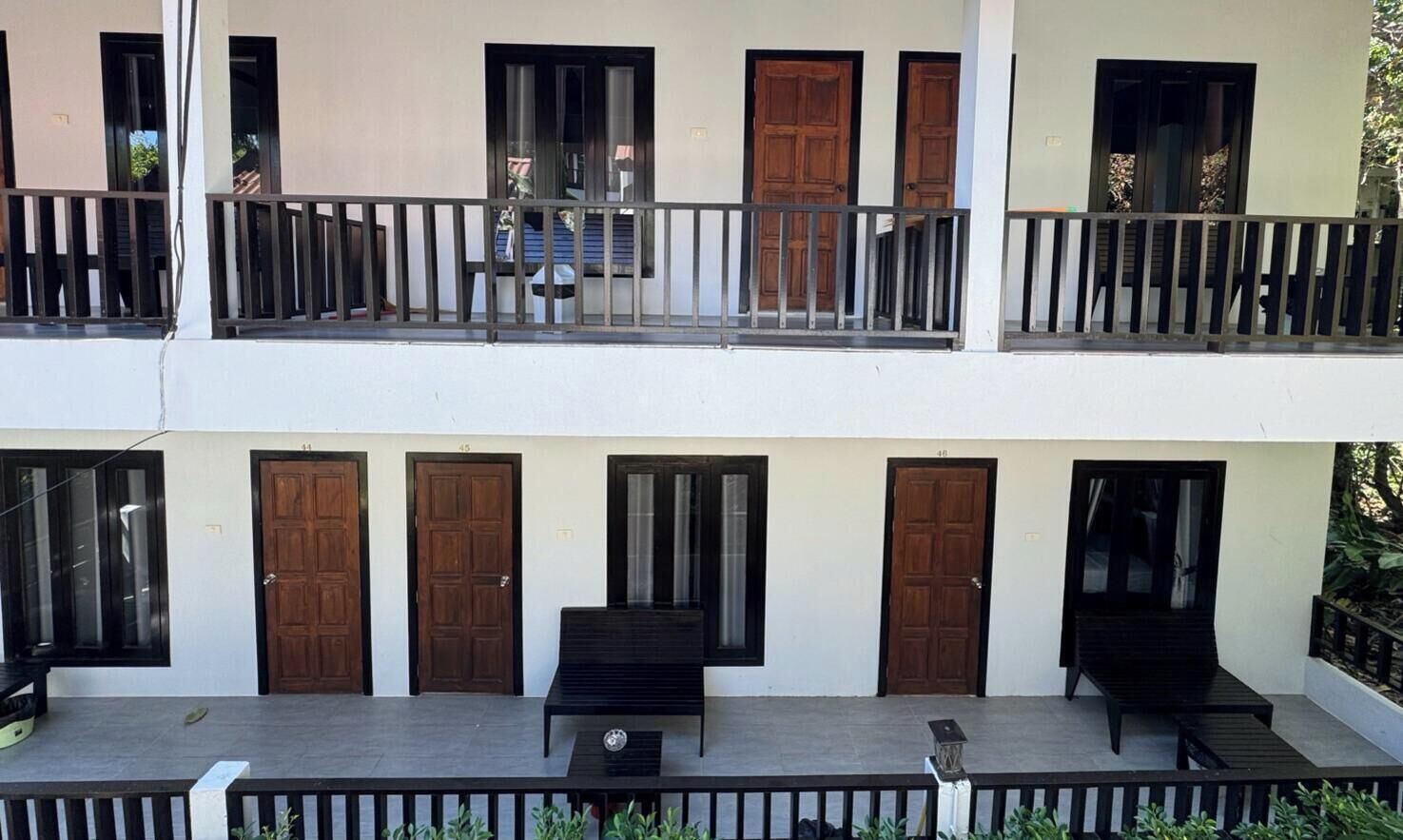 A two-story building with balconies, wooden doors, and a patio area with seating.