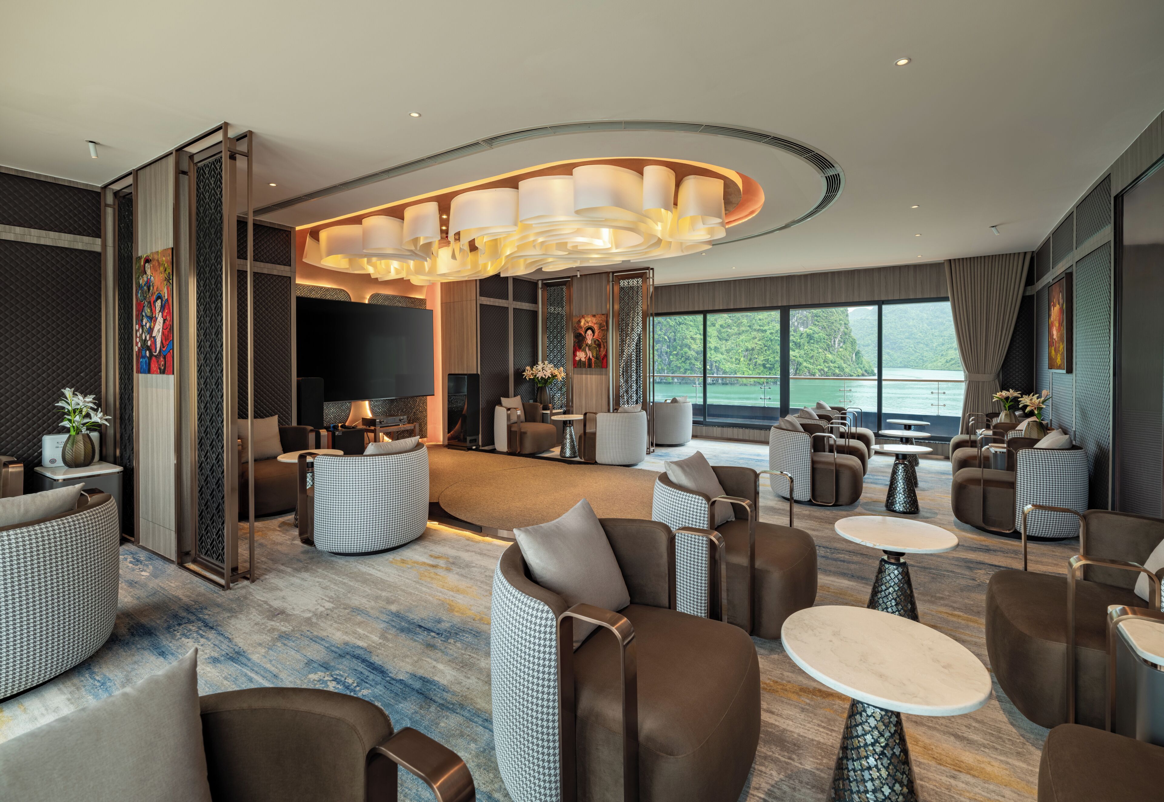 A modern hotel lobby with seating areas, a television, and large windows overlooking a body of water.