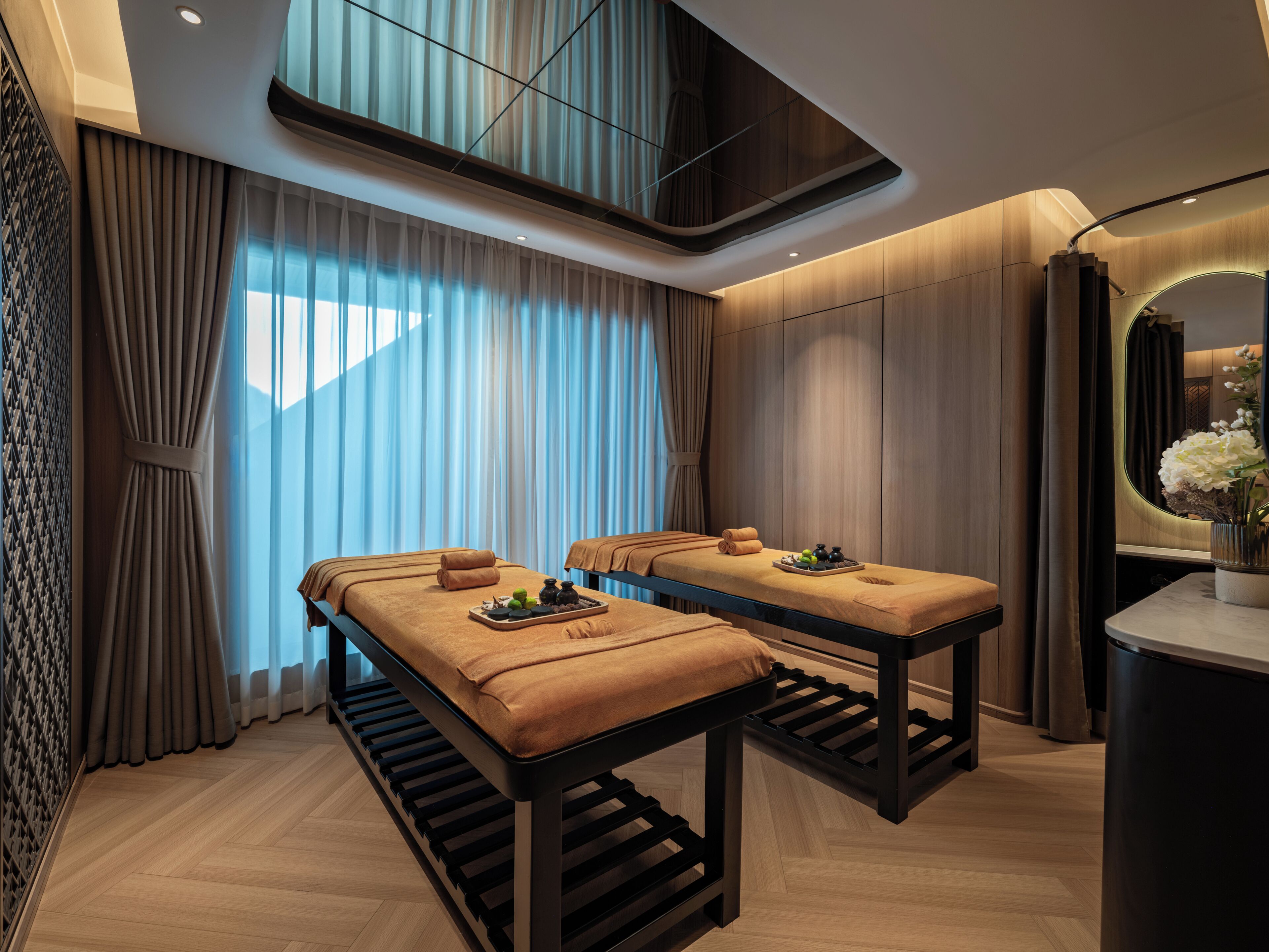 Une salle de spa équipée de deux tables de massage, d’un miroir et d’un plancher en bois.