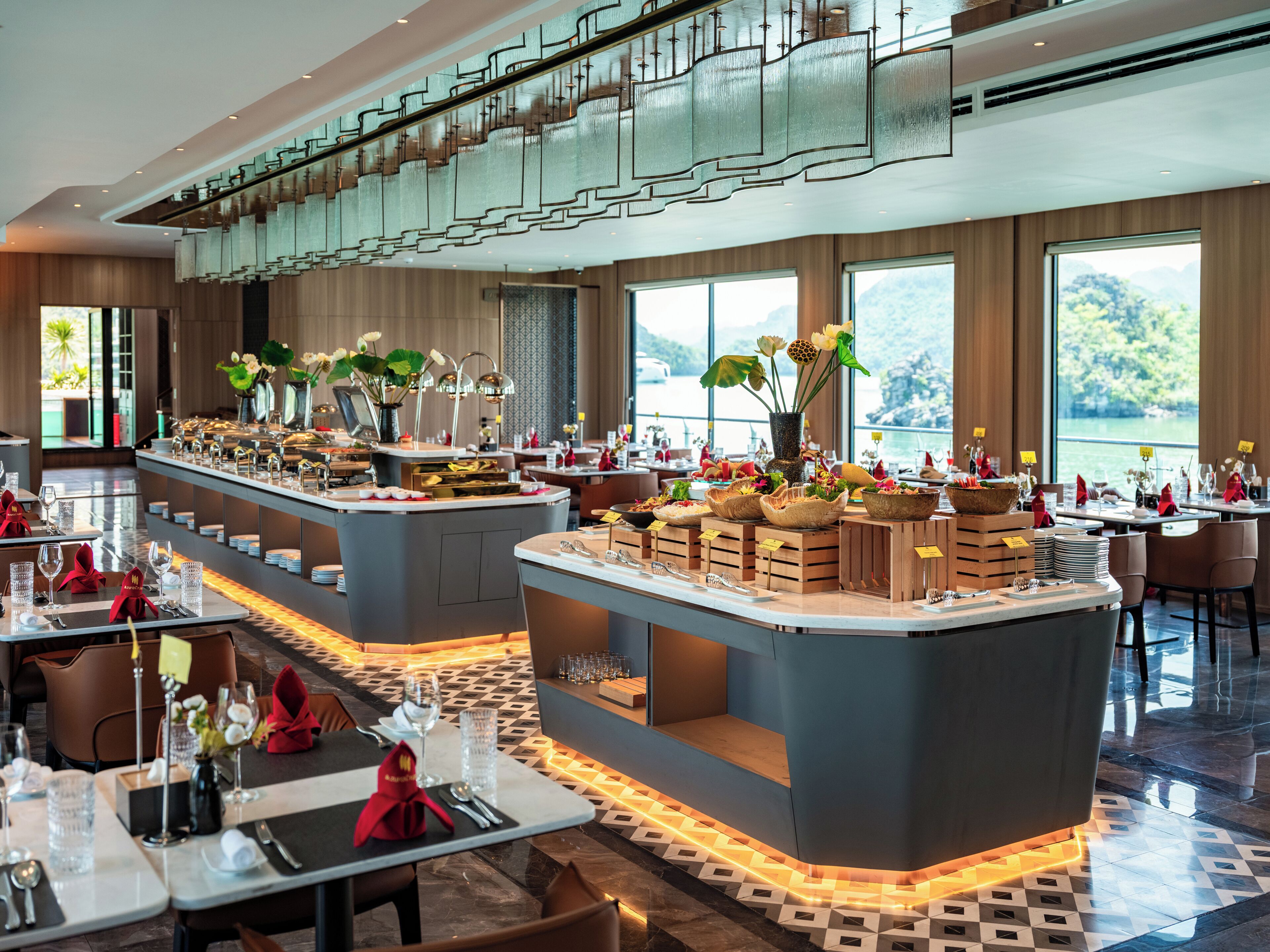Ein modernes Restaurant mit einer zentralen Kochinsel, mehreren Esstischen und großen Fenstern mit Blick.