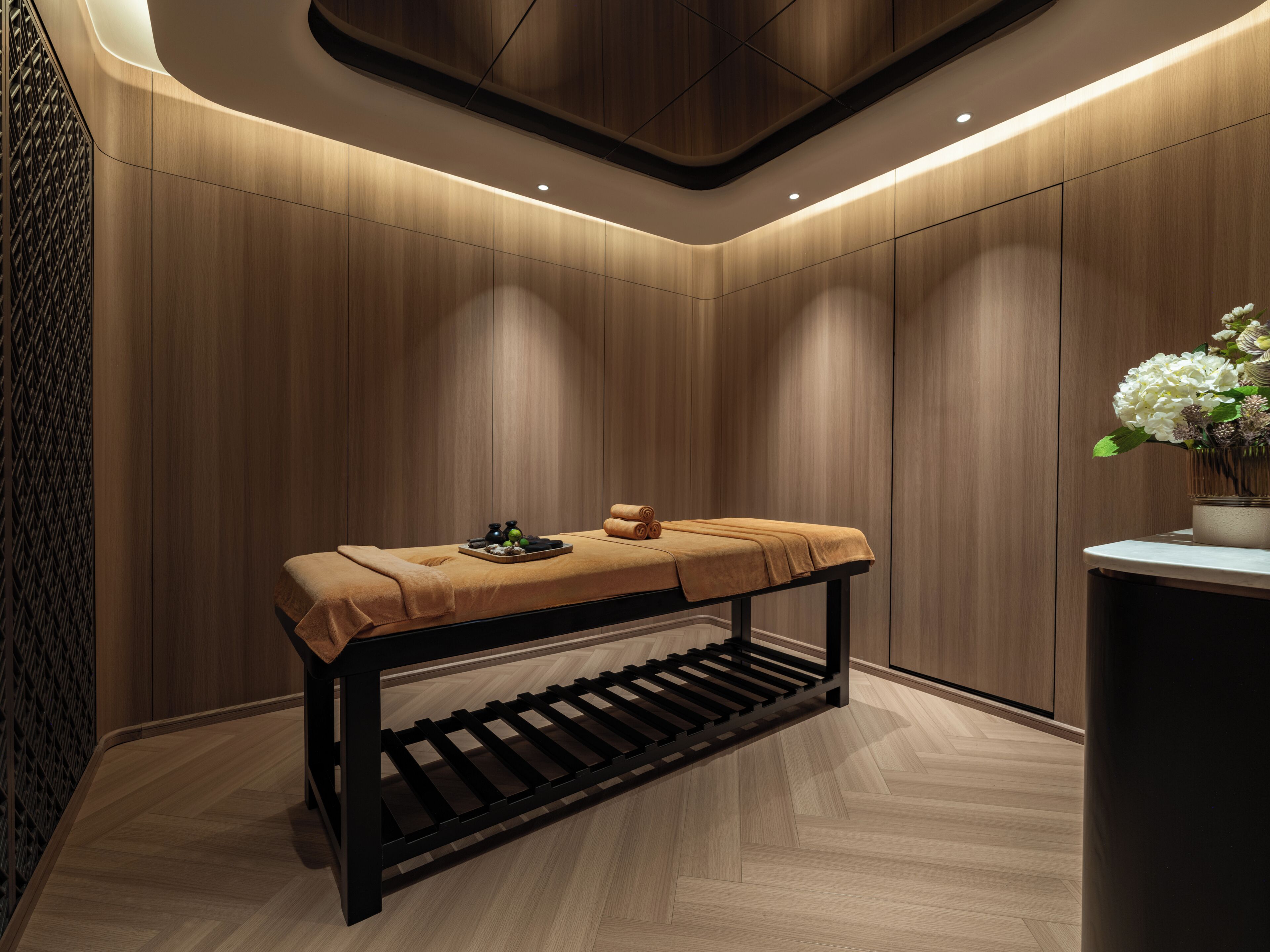 Ein moderner Spa-Bereich mit einer Holzbank, einer Ablage für Annehmlichkeiten und einem Blumenstrauß.