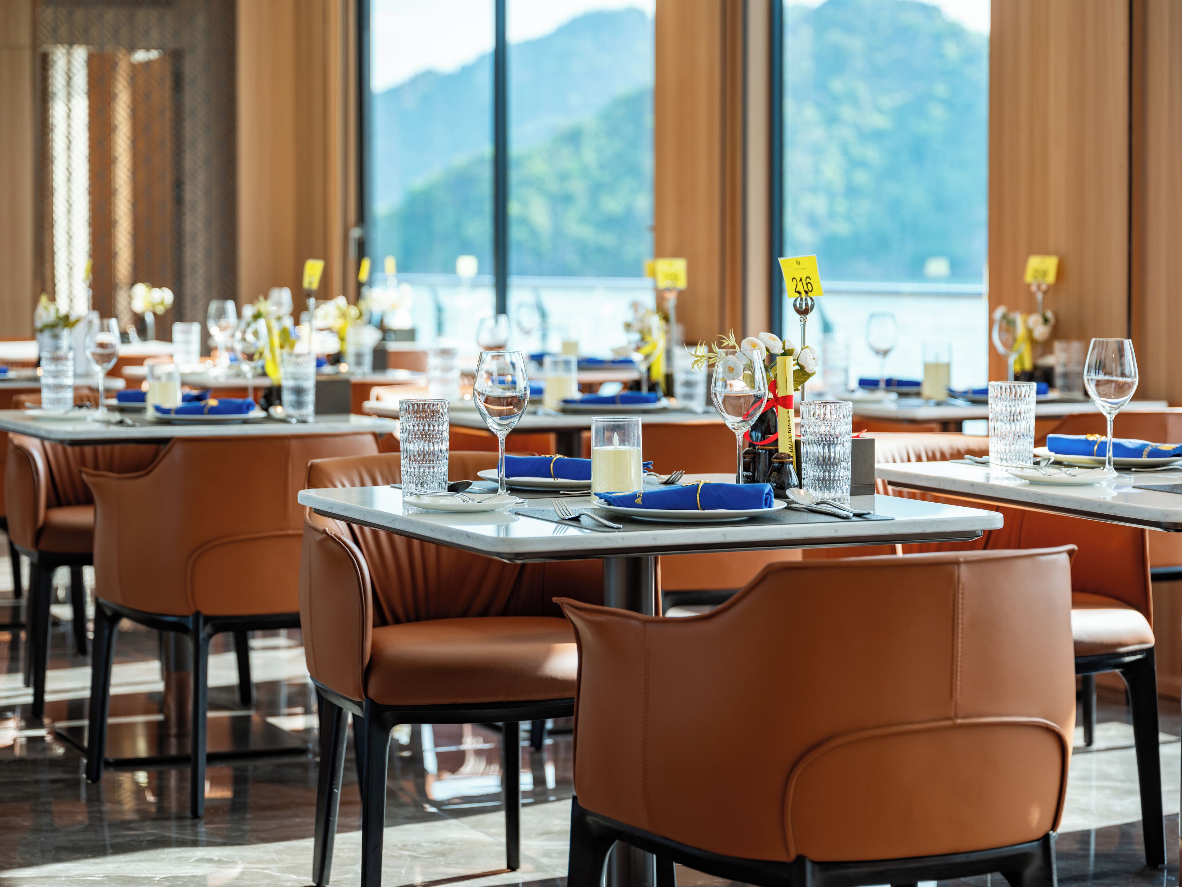 A restaurant with tables set for dining, featuring a view of mountains through large windows.