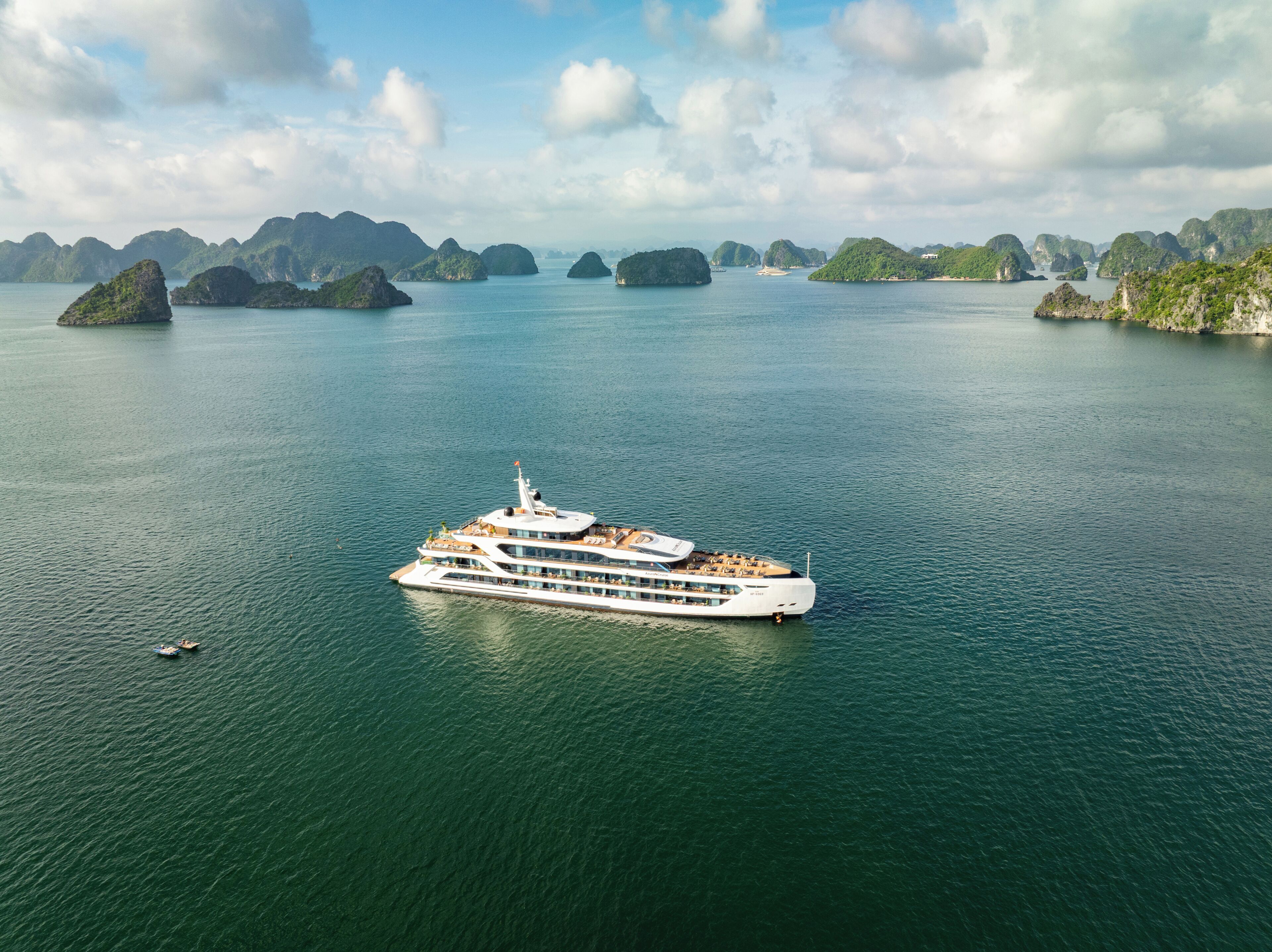 A large cruise ship with multiple decks and a white hull, floating in calm waters with green islands in the background.