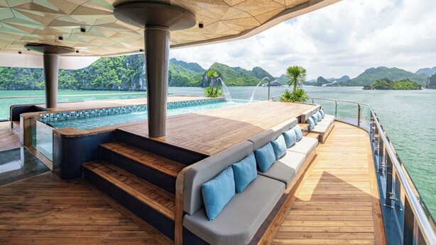 Une terrasse avec une piscine, des sièges et une vue sur un plan d’eau bordé de montagnes.