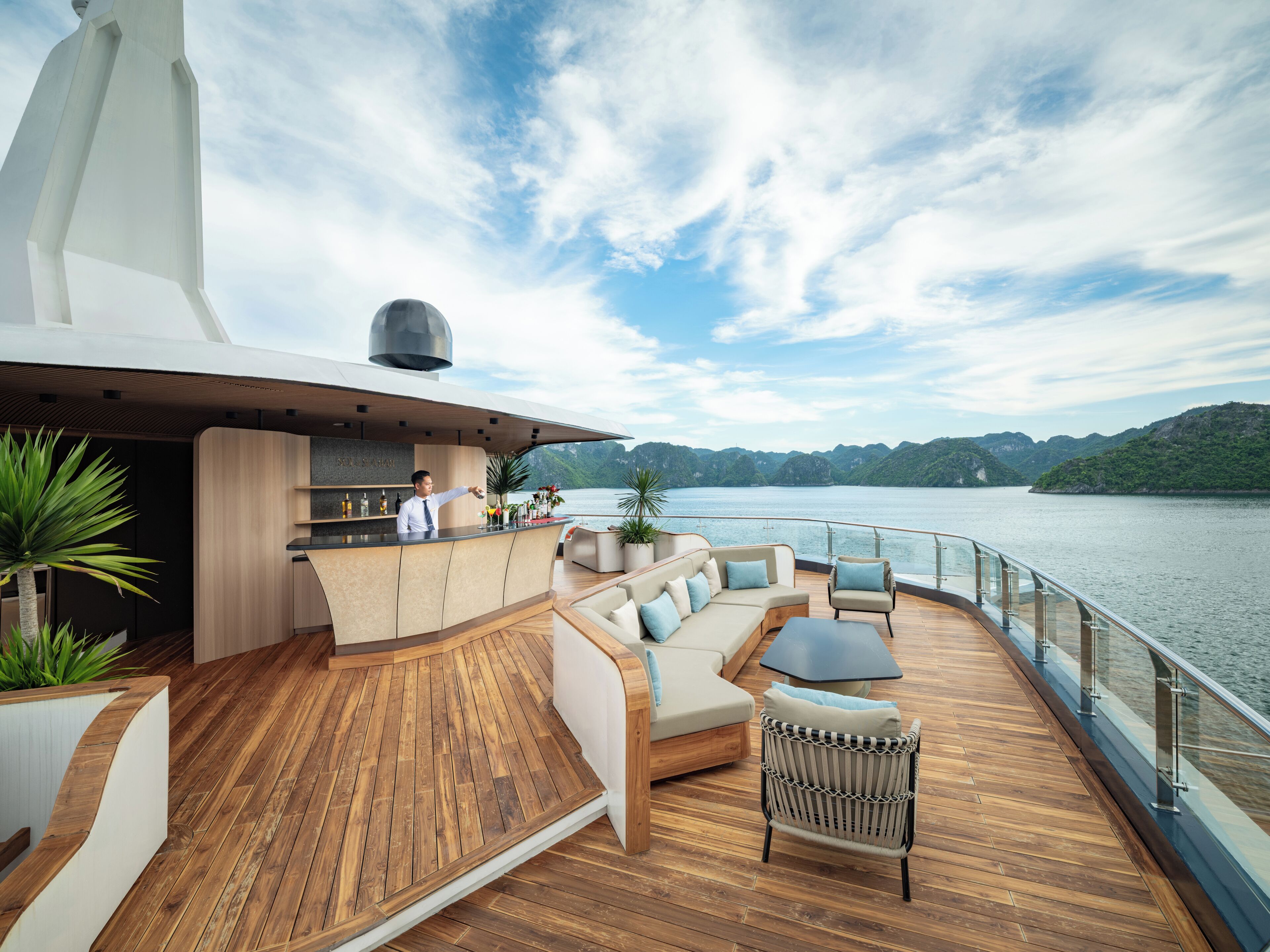 A modern outdoor bar area with a bar counter, seating, and a view of a lake.