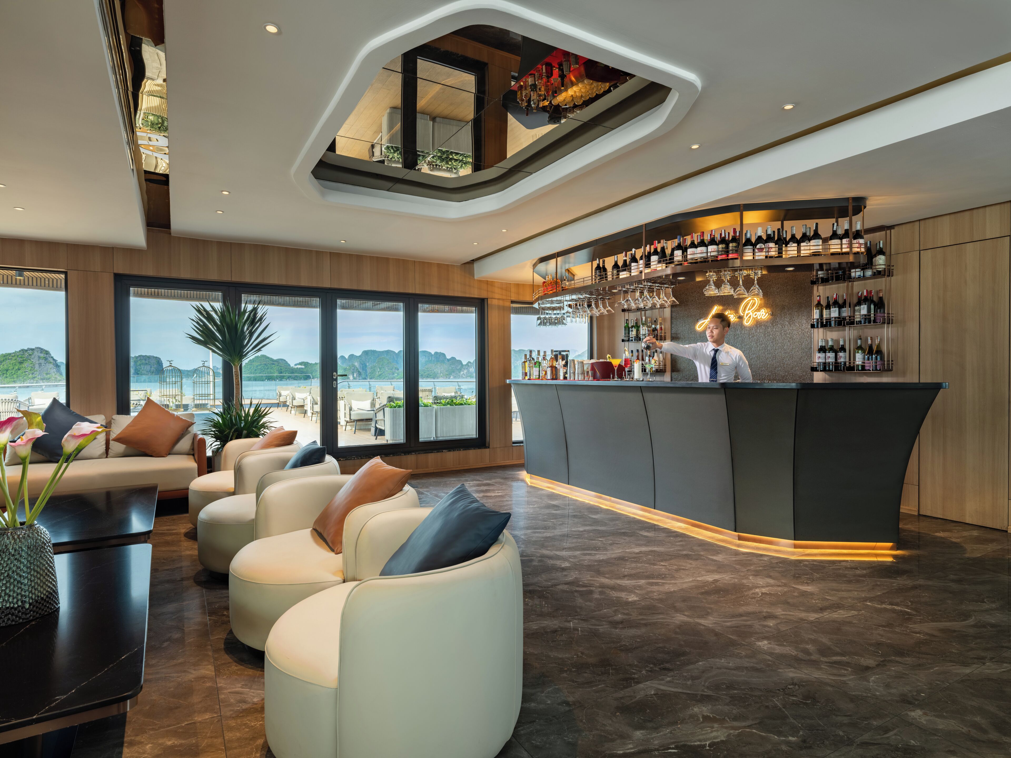 A modern bar area with a bartender, seating with a view, and a variety of bottles and glasses.