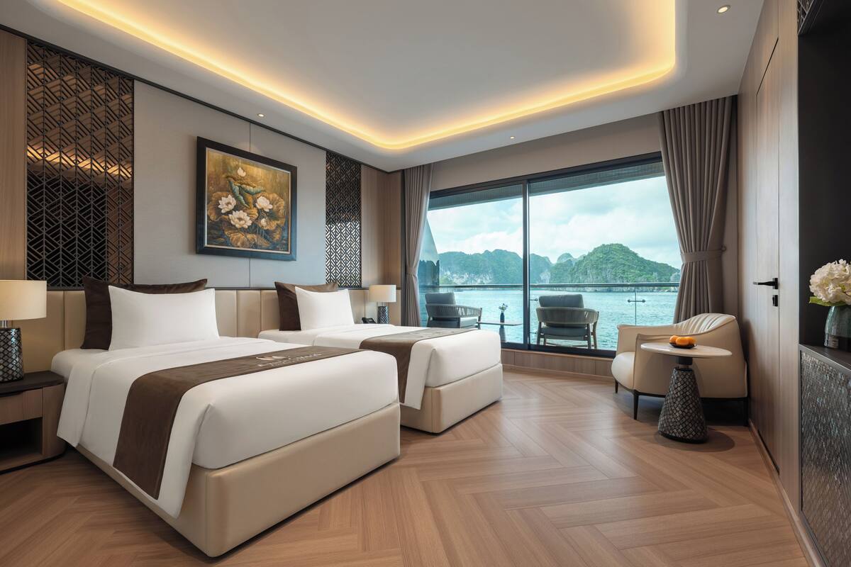 A modern hotel room with a large bed, two bedside tables, a seating area with chairs, and a large window offering a view of the water.