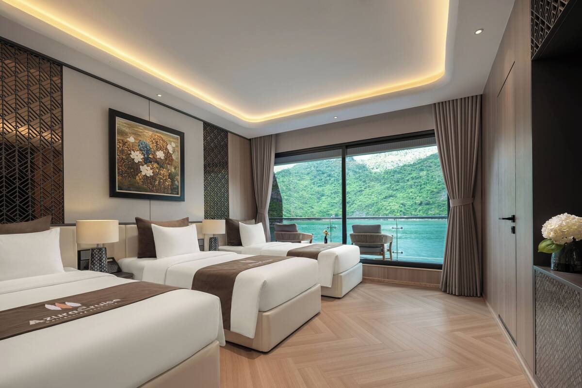 A modern hotel room with two beds, a large window with a view of a body of water, and a balcony.