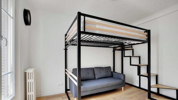 Ein Etagenbett mit grauem Schlafsofa, Holzböden, Radiator und Holzfußboden in einem Raum mit weißen Wänden.