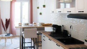 Eine moderne Küche mit weißen Schränken, einer schwarzen Arbeitsplatte und einem eingebauten Herd. Ein Fenster mit rosa Vorhängen und eine hängende Pflanze sind ebenfalls vorhanden.